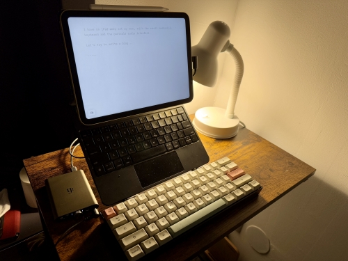 A tiny desk in a dimly-lit corner. There's an iPad, a mechanical keyboard, and a portable DAC. • Header image for: My Setups Part One - Writing This • Here, I talk about one of my setups (part one) • Ayo's Blog • Blogs on tech, life, and personal growth • Ayo Ayco